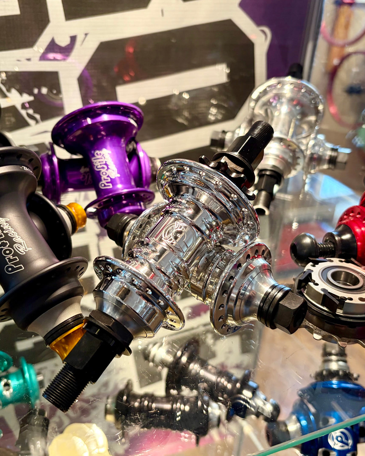 A close-up display of various bicycle hubs in different colors, including black, purple, red, silver, and blue, arranged on a glass surface.