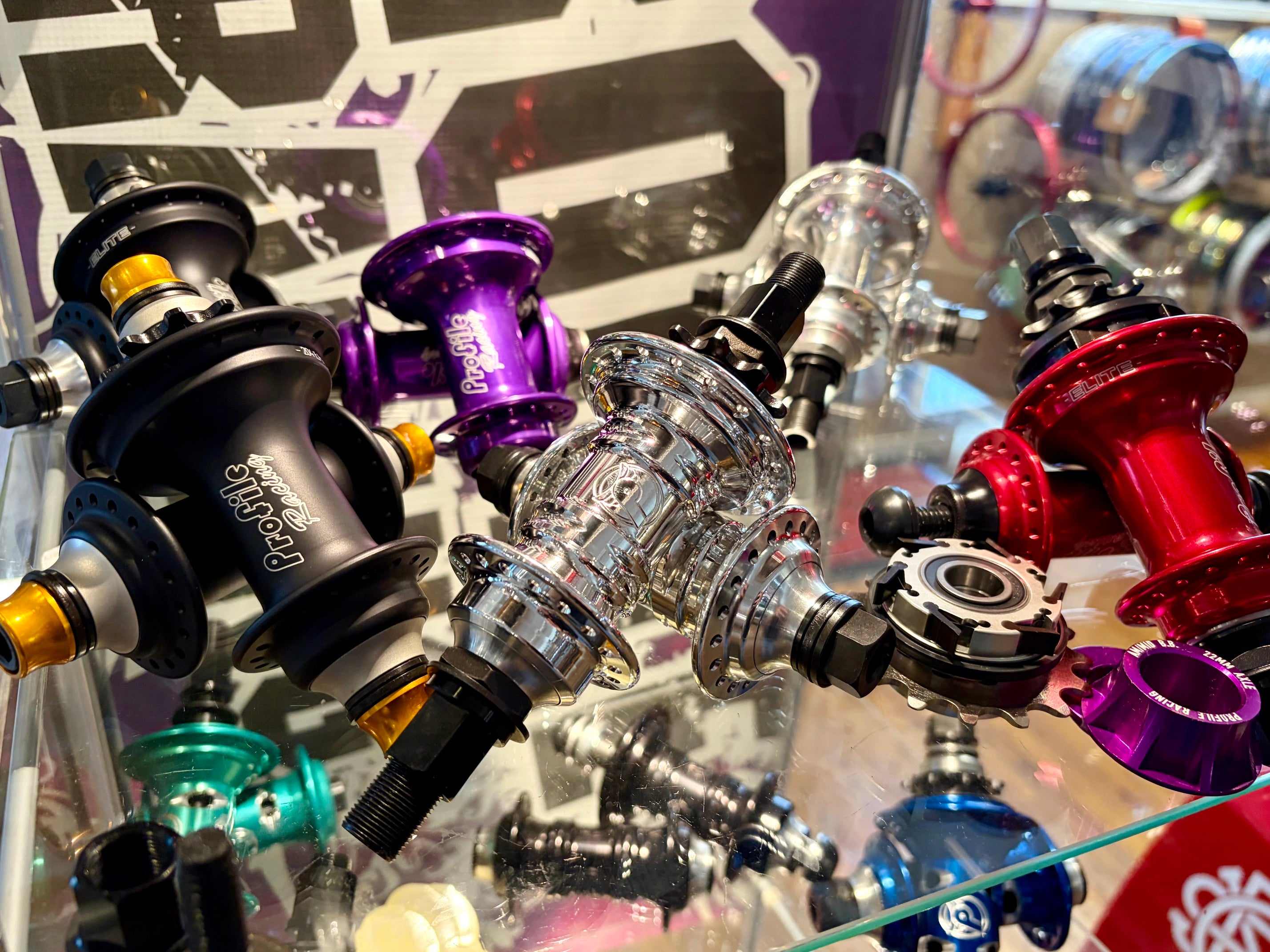 A close-up display of various bicycle hubs in different colors, including black, purple, red, silver, and blue, arranged on a glass surface.