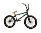 A dark green BMX bike with a tan seat and black handlebars, positioned in profile against a yellow cardboard wall with the brand name 'Sunday' printed on it.